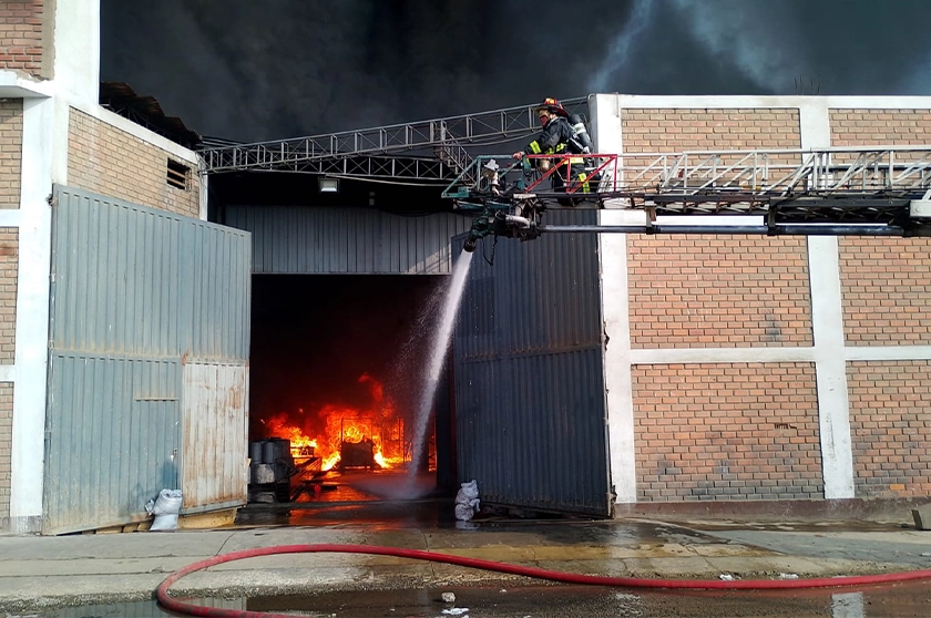Bomberos con manguera echando agua a incendio en planta industrial de Ate